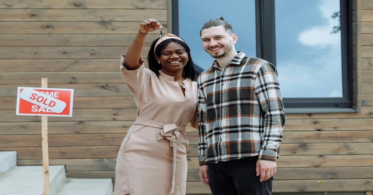 a happy couple standing in front of a house with keys featured image for how much house can I afford